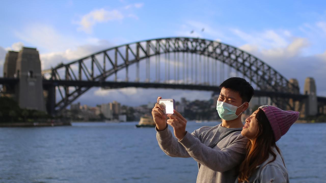 People wear face masks in front of the Sydney Harbour Bridge in Sydney. Pictur: AAP /Steven Saphore