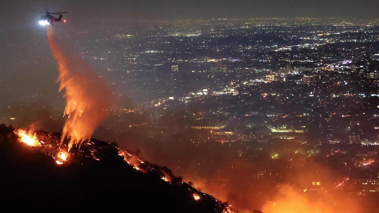 A firefighting helicopter drops water as the burns in the Hollywood Hills. (Photo by MARIO TAMA/Getty Images via AFP)