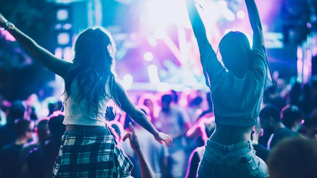 Back view of carefree women having fun while being on man's shoulders during music festival.