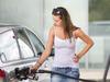 Attractive, young woman refueling her car in a gas station, checking the amount of gas, disliking the price tag and the gas mileage of her engine