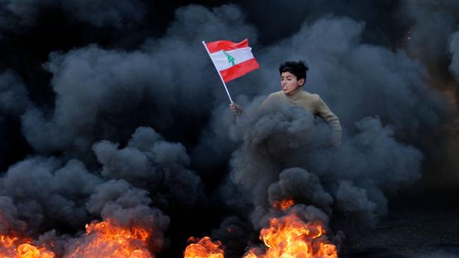 A Lebanese youth runs with the national flag as smoke billows during a protest in Beirut. Picture: AFP.