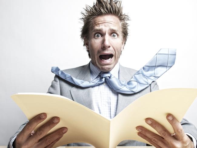 Office worker looks at the camera with expression of fear as he opens a file folder at his desk