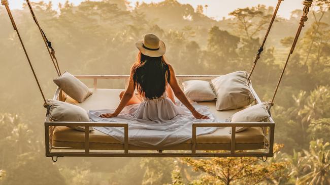 Photo of a young woman sitting on the swing.  Jungle Bed hanging over the tropical forest with Caucasian female resting while looking at the view, Bali, Indonesia. Rear view of a female sitting and enjoying the view.Escape 19 May 2024Doc HolidayPhoto - iStock