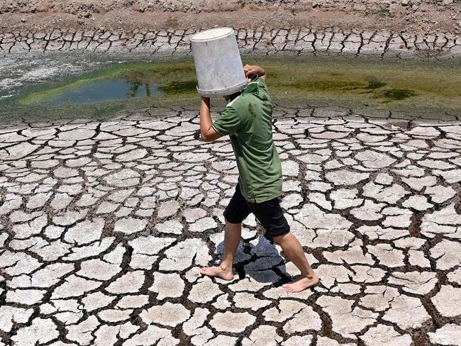 TOPSHOT - A man carries a plastic bucket across the cracked bed of a dried-up pond in Vietnam's southern Ben Tre province on March 19, 2024. Every day, farmer Nguyen Hoai Thuong prays in vain for rain to fall on the cracked dry earth of her garden in Vietnam's Mekong Delta -- the country's "rice bowl" agricultural heartland.A blazing month-long heatwave has brought drought, parching the land in Thuong's home of Ben Tre province, 130 kilometres (80 miles) south of business hub Ho Chi Minh City. (Photo by Nhac NGUYEN / AFP)