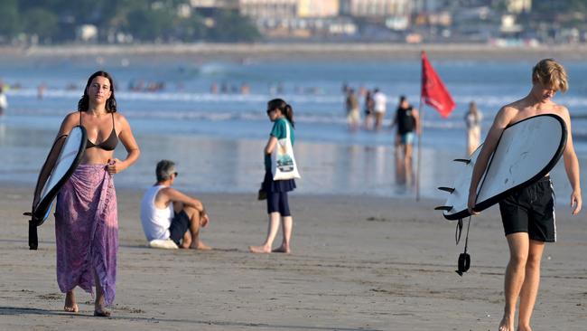 Foreign tourists carry their surfboard as they walk along Kuta beach near Denpasar, on Indonesia's Bali island on August 3, 2024. (Photo by SONNY TUMBELAKA / AFP)