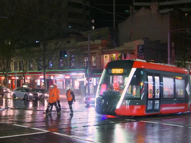 Workers walk alongside a tram travelling along George St for the first time in more than 60 years.