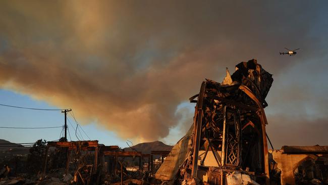 The Palisades Fire continues to burn above the remains of Community United Methodist Church, with a police helicopter flying past as wildfires cause damage and loss. Picture: Getty