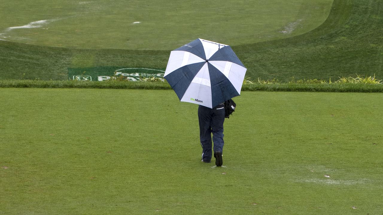 A man holding an umbrella walks on the course after BMW Championship golf tournament was cancelled due to inclement weather.