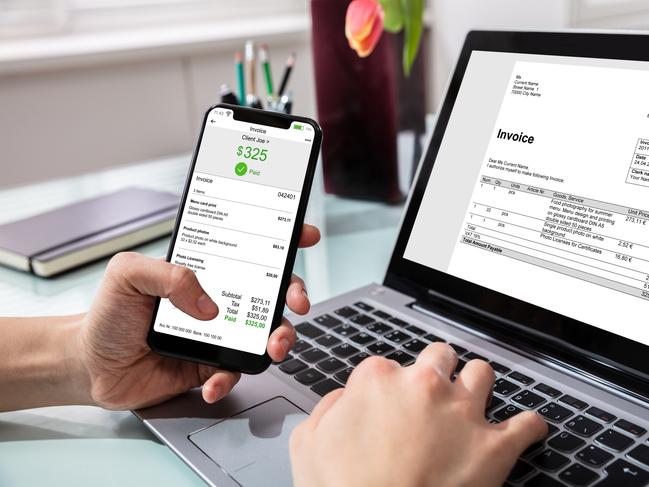 Close-up Of Businessperson Using Laptop While Paying Invoice On Mobilephone In Office