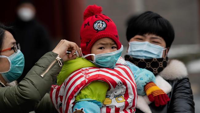 A woman, left, puts a protective mask on a child at the Jingshan park in Beijing in February. Picture: Nicolas Asfouri/AFP