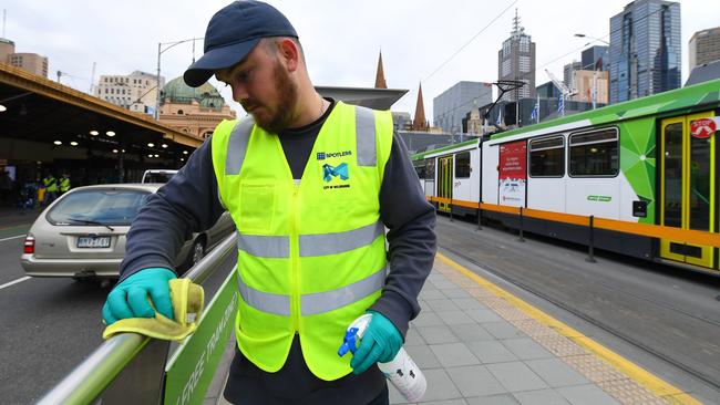 A member of a cleaning team wipes down the tram stop on Swanston St outside Flinders St Station. Picture: AAP