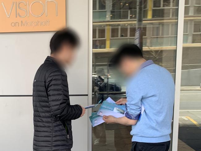 Two people with a pile of opened council election ballot papers outside a city student accommodation building.