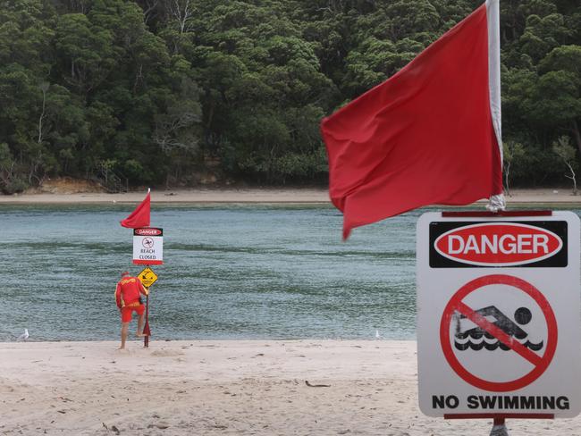 A lifeguard puts up warning signs on Tallebudgera Creek beach after stormwater outflows pollute the pristine waters with debris, causing a hazard to swimmers. Picture Glenn Hampson