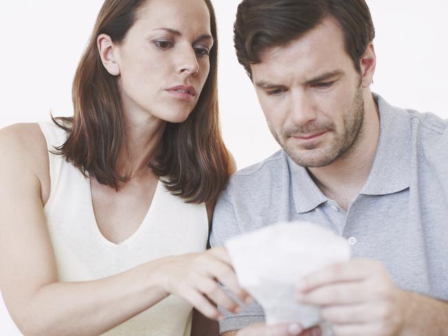 A married couple looking slightly concerned as they inspect bills and discuss their home finances