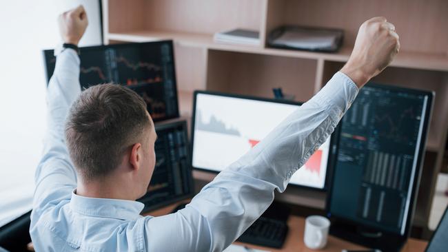 Hands up because of success. Man working online in the office with multiple computer screens in index charts.. happy investor generic