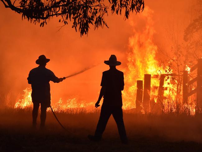 Residents defend a property from a bushfire at Hillsville near Taree on Thursday. Scientists says the shoulders of the peak fire period are expanding. Picture: Peter Parks/AFP