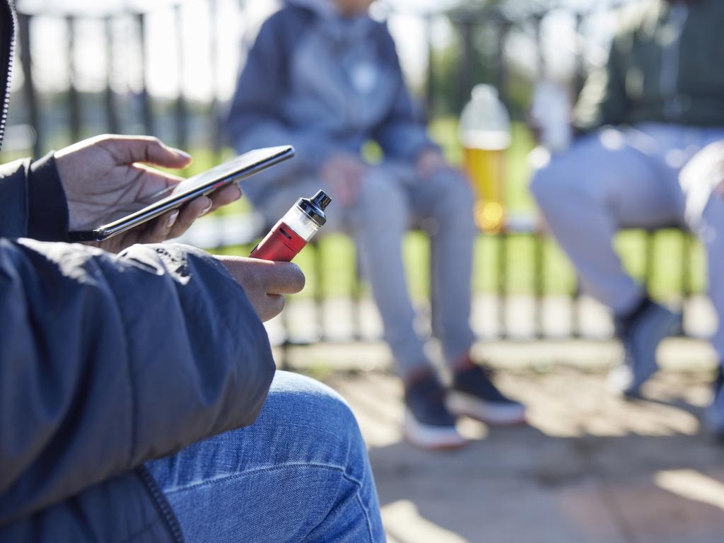 Close Up Of Teenagers With Mobile Phone Vaping and Drinking Alcohol In Park Picture: iStock