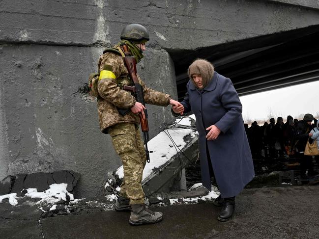 A Ukrainian soldier helps an elderly woman to cross a destroyed bridge as she evacuates the city of Irpin. Picture: AFP