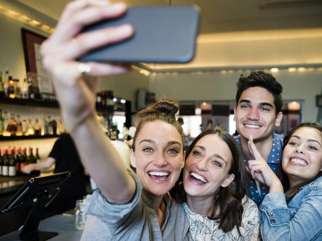 Four people in bar taking photo of themselves on smartphone in bar. Woman holding camera phone with friends smiling and posing, having fun  Picture: iStock