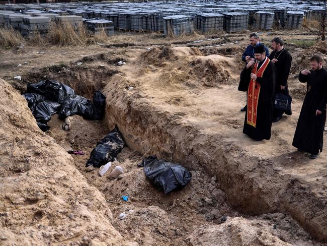 Priests pray over body bags in a mass grave in the grounds surrounding the St Andrew church in Bucha. Picture: AFP