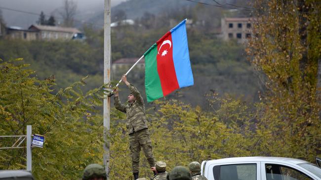 An Azerbaijani soldier fixes a national flag on a lamp post in the town of Lachin on December 1. Picture: Karen Minasayan/AFP