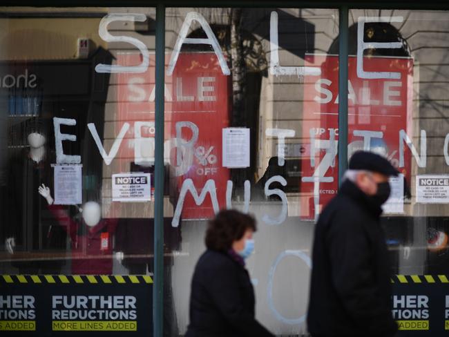 Pedestrians wearing masks because of the coronavirus pandemic walk past a closed store with a sale sign on the window on the high street in Maidstone, southeast England. Picture: AFP