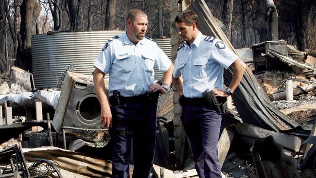 Leading Senior Constable Cameron Caine and Roger Wood stand among the ruins of a Kinglake property in the wake of the Black Saturday bushfires.