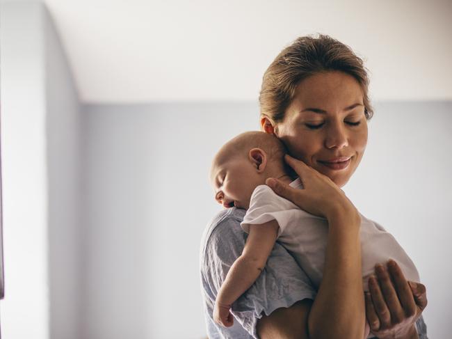 A happy new mother smiles as she craddles her sleeping baby in her arms. She has her eyes closed as she holds her close.