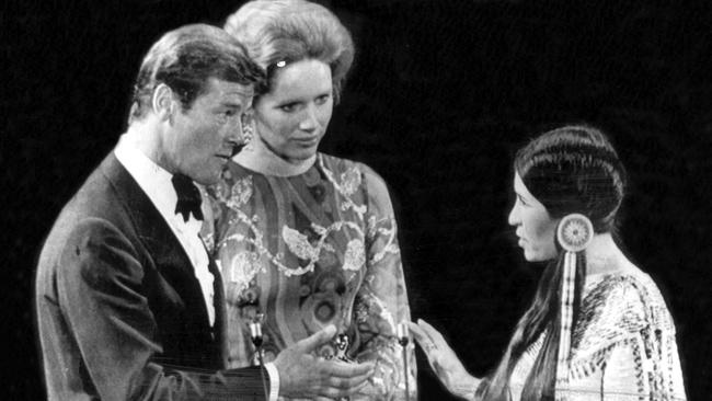 Sacheen Littlefeather holds her hand out to Liv Ullmann and Roger Moore to refuse the Oscar for actor Marlon Brando, who won the coveted award for his part in The Godfather.