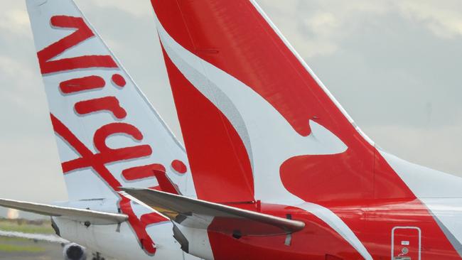 The vertical stabilisers of a Qantas Boeing B737-838 plane, registration VH-VZQ, and a Virgin Australia Boeing B737-8FE plane, registration VH-VUZ, waiting at the northern end of the main runway of Sydney Kingsford-Smith Airport in preparation for departure.  The Qantas plane is heading to Adelaide as flight QF741 and the Virgin plane is heading to Adelaide as flight VA428.  In the background is another Virgin B737-8FE plane. This image was taken from Nigel Love Bridge, Mascot on a sunny afternoon on 3 December 2023.