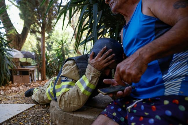 An Israeli firefighter and a resident take cover as sirens warn of rockets launched from southern Lebanon, in Kiryat Shmona, northern Israel