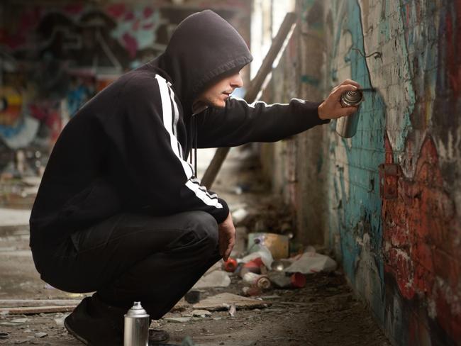 Illegal Young man Spraying black paint on a Graffiti wall. (room for text)