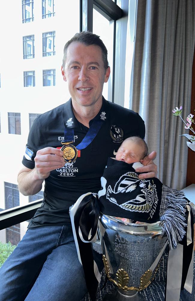 Collingwood premiership coach Craig McRae, his baby daughter Maggie, and the premiership cup. Picture: Supplied