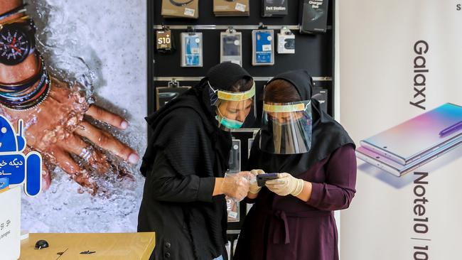 Iranian women wearing personal protective equipment look at mobile phones in a store in Mashhad. Picture: AFP
