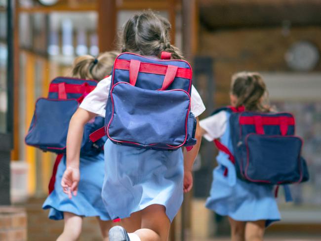 Rear view of excited students running towards entrance. Girls are carrying backpacks while leaving from school. Happy friends are wearing school uniforms. Source: iStock