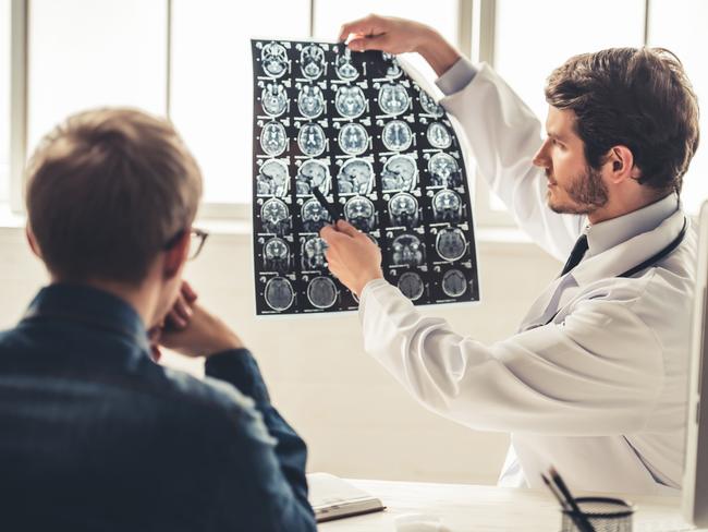 Gold Coast Suns - My Life - Tasman Oncology Research.Handsome young doctor in white coat is showing x-ray image to his patient while working in office