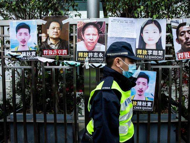 TOPSHOT - A police officer walks past placards of detained rights activists taped on the fence of the Chinese liaison office in Hong Kong on February 19, 2020, in protest against Beijing’s detention of prominent anti-corruption activist Xu Zhiyong. - Police in China have arrested Xu Zhiyong, a prominent anti-corruption activist who had been criticising President Xi Jinping’s handling of the COVID-19 coronavirus. (Photo by ISAAC LAWRENCE / AFP)