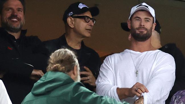 Jeff Goldblum (black Bunnies cap) talks to Chris Hemsworth (in white) and Russell Crowe (back to camera) at the Rabbitohs v Roosters match. Picture: Cameron Spencer/Getty Images