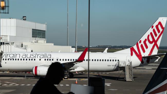 A man sits at a cafe in front of a Virgin Australia aircraft at Sydney Airport, Sydney, Friday, June 19, 2020. Picture: AAP