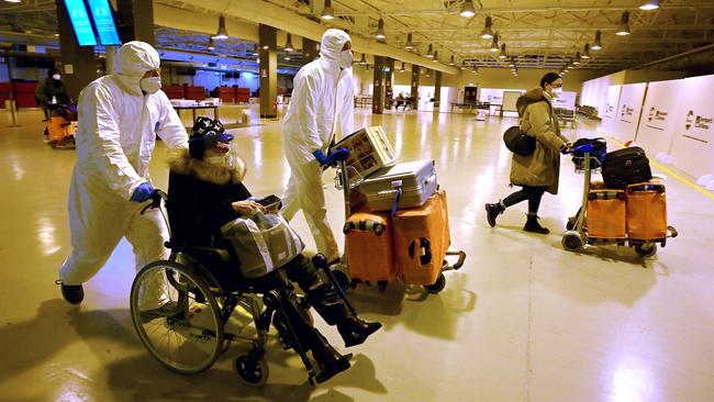 Workers wearing protective masks and suits help Chinese travellers leaving the arrival hall of Rome’s Fiumicino airport on Thursday. Picture: AFP