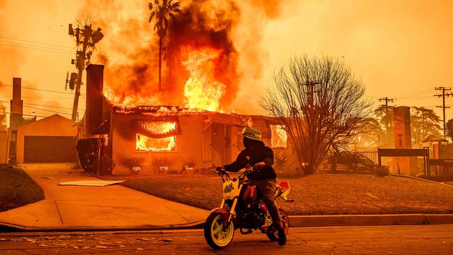 A motorcyclist stops to look at a burning home during the Eaton fire in the Altadena area of Los Angeles county, California. Picture: AFP