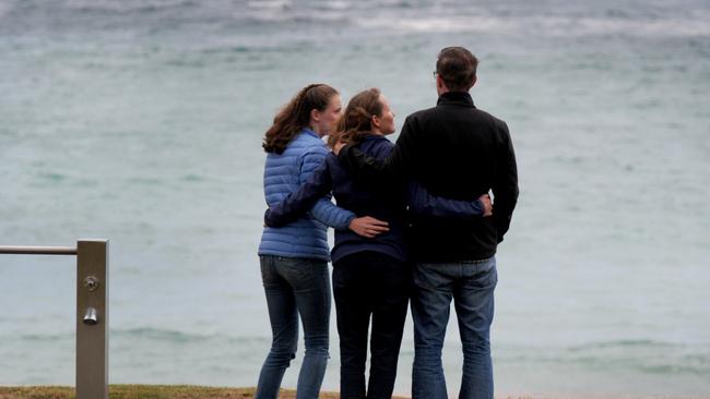 A trio gathers to mourn the two lifesavers who drowned at the beach. Picture: Andrew Henshaw