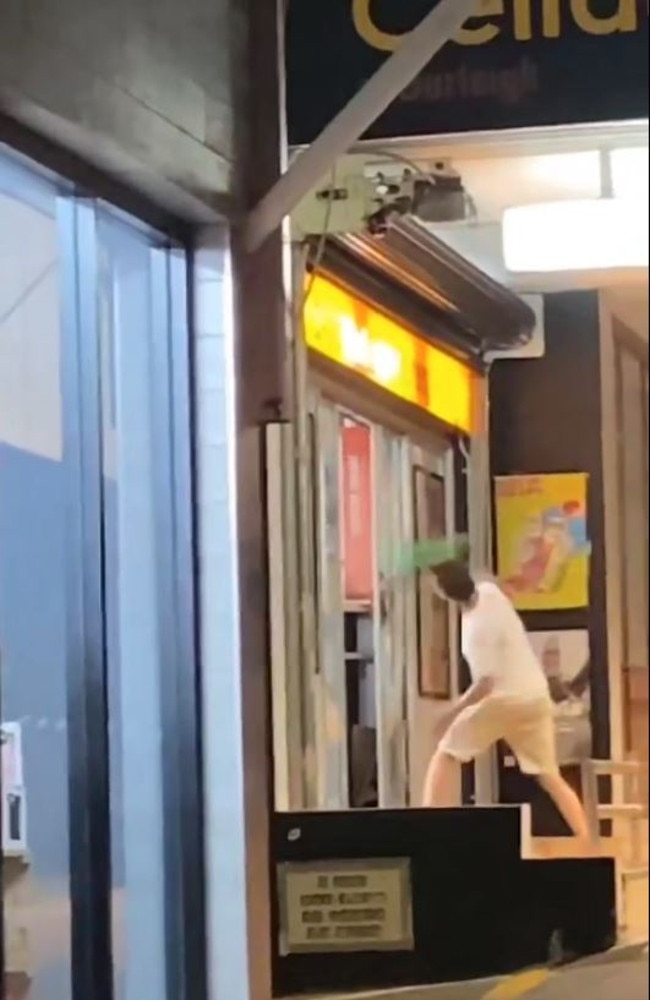 A man smashing a helmet against the front of the Cellarbrations bottle shop on West St in Burleigh.