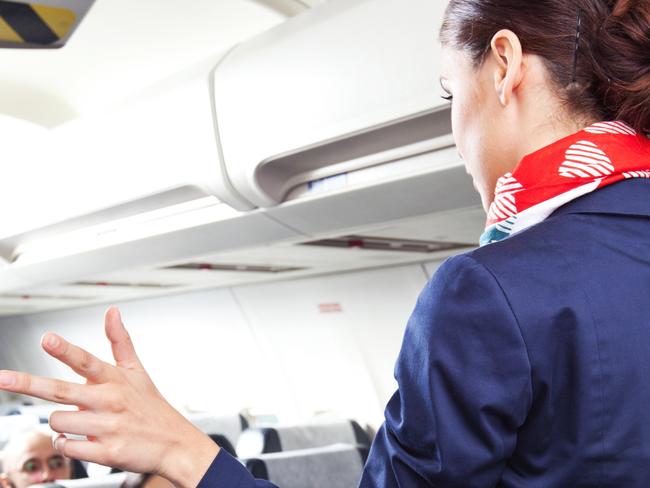 Back view of flight attendant standing in an airplane and demonstrating a emergency exits before taking off. Picture: iStock.