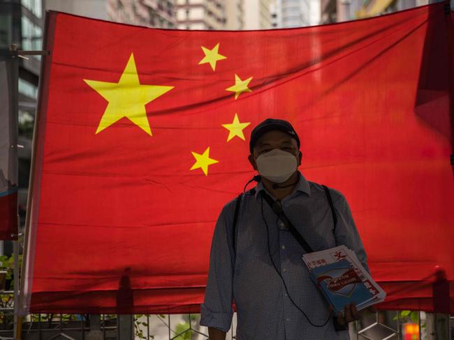 A pro-government supporter hands out newspapers in front of a Chinese national flag in Hong Kong on July 1, 2020, on the 23rd anniversary of the city's handover from Britain to China. - Hong Kong marks the 23rd anniversary of its handover to China on July 1 under the glare of a new national security law imposed by Beijing, with protests banned and the city's cherished freedoms looking increasingly fragile. (Photo by DALE DE LA REY / AFP)