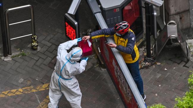 A worker wearing protective gear receives an item from a delivery worker at the entrance of a compound during the second stage of a pandemic lockdown in Jing' an district in Shanghai. Picture: AFP