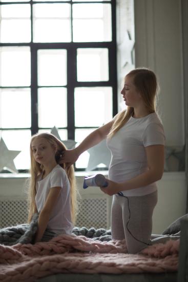 Beautiful mother takes care of her teenage daughter. Mother dries hair with a blow-dryer daughter. Mother and daughter with long blond hair,  concept of tenderness and mutual understanding