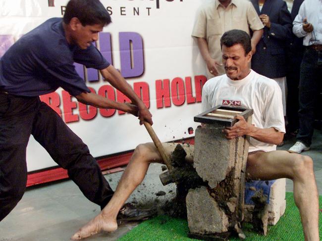 ATTENTION EDITORS - CAPTION CLARIFICATION Nilesh Parida (L), a black belt in karate, uses a 6.5 kg (14.3 lb) hammer to smash three concrete slabs against the groin of Indian freelance journalist Bibhuti Nayak during an adventure television channel invitation to persons wanting to set a record, in Bombay July 13, 2002. Nayak is already featured in the Guinness Book for doing 819 back-hand push ups in an hour. His earlier request to have the act of having been kicked 43 times in the groin without an abdominal guard was turned down by the British annual. REUTERS/Arko Datta - RTR7LKX