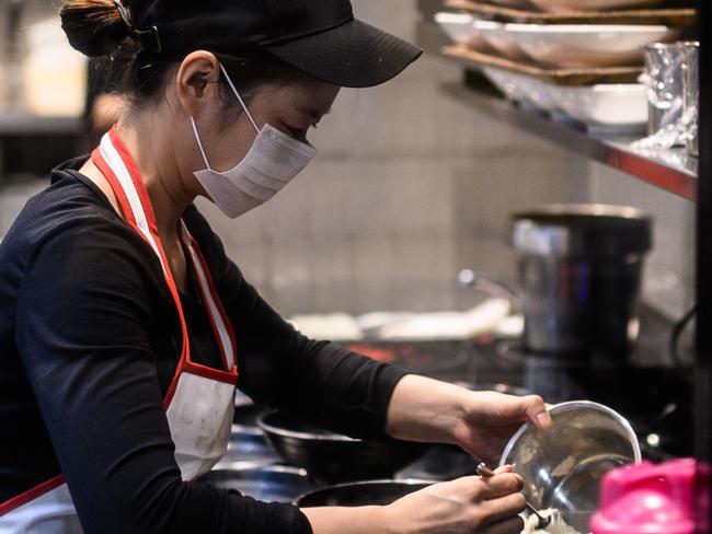 A woman seen wearing a protective face mask in a restaurant kitchen in Sydney, Monday, March 16, 2020. (AAP Image/James Gourley) NO ARCHIVING