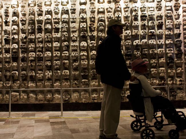 Writ in stone ... A man pushes a woman in a wheelchair past a wall of ancient stone skulls, excavated at Templo Mayor, that represent sacrificial victims. Source: AP